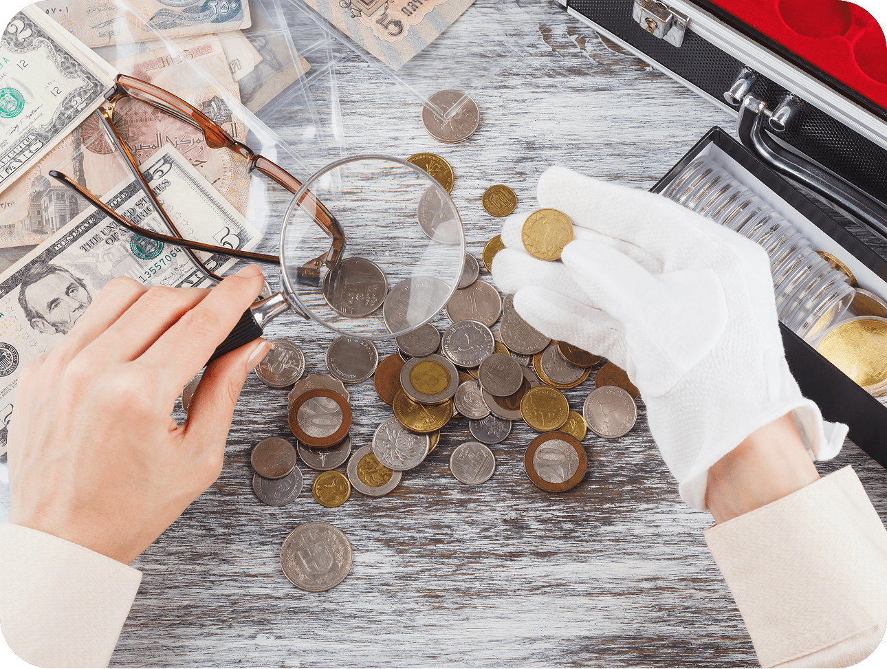 Person examining coins with magnifying glass.